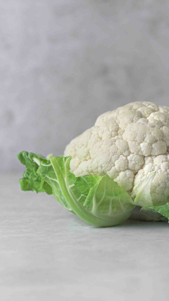 Frischer Blumenkohl mit grünen Blättern auf hellem Untergrund.