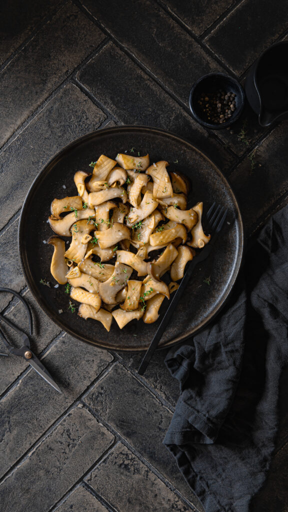 Food-Fotografie von gebratenen Kräuterseitlingen mit frischem Thymian – Moody-Stil mit natürlichem Licht, Textur und dunklem Untergrund